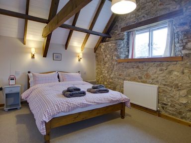 A bedroom with a double bed with plaid bedding and towels on top with exposed wooden beams and stone walls at Whitcombe Cottage in Honiton