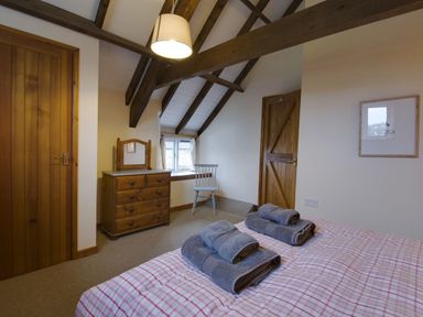 A bedroom with wooden doors dresser and chair with towels on bed at Whitcombe Cottage in Honiton