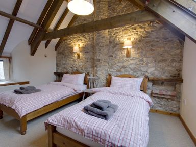 A bedroom with two single beds with checked bedding and a stone wall at Whitcombe Cottage in Honiton