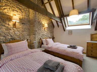 A bedroom with two single beds with plaid bedding and folded towels on each bed a wooden dresser a chair stone wall and a skylight window at Whitcombe Cottage in Honiton