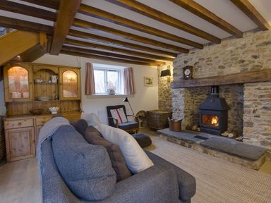 A living room with a stone fireplace wood stove wooden cabinet armchair and sofa at Whitcombe Cottage in Honiton