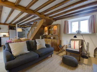 Living room with grey sofas and armchair near a window and wooden cabinet with stairs in background at Whitcombe Cottage in Honiton