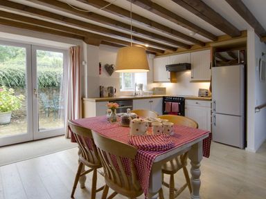 A kitchen with wooden table and chairs a red checkered tablecloth and white cabinets at Whitcombe Cottage Honiton