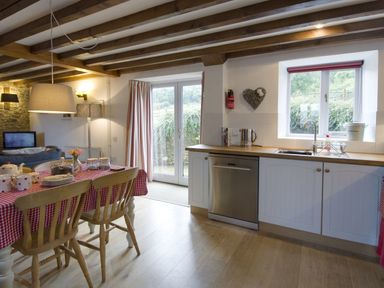 A kitchen and dining area with wooden chairs and a table covered with a red checkered cloth at Whitcombe Cottage in Honiton