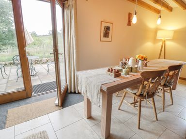 A dining room with a wooden table set with mugs plates and eggs next to glass doors leading to a patio at Swallows Cottage in Honiton