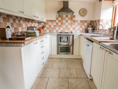 A kitchen with white cabinets tiled backsplash oven sink and countertop appliances at Swallows Cottage in Honiton