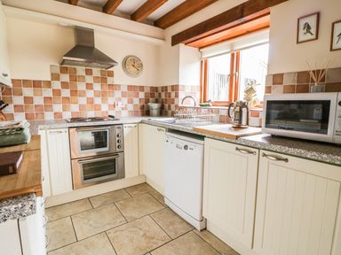 A kitchen with stove oven microwave dishwasher and window with wooden beams at Swallows Cottage in Honiton
