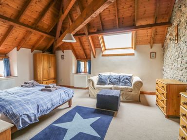 A bedroom with a wooden ceiling beams a double bed a blue star rug a sofa and wooden furniture at Swallows Cottage in Honiton
