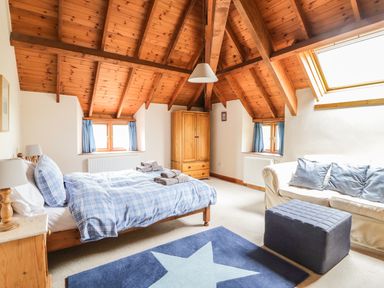 A bedroom with a wooden bed a blue star rug a sofa and a wooden wardrobe at Swallows Cottage in Honiton