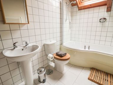 A bathroom with a sink mirror toilet with wooden lid and towel bathtub with shower at Swallows Cottage in Honiton