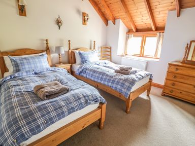 A bedroom with two single beds blue plaid bedding wooden furniture and a window at Swallows Cottage in Honiton