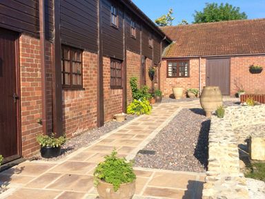 A brick and wood exterior courtyard with potted plants and large urns at The Linney in Colyton