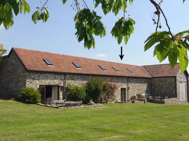 An exterior view of a stone barn with a tiled roof and outdoor seating on grass at The Linney in Colyton