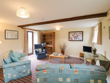 A living room with patterned sofas a wooden bookshelf and a small television at The Linney in Colyton
