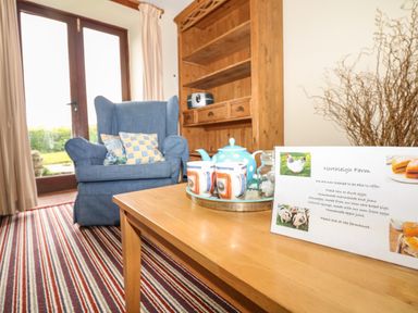 A sitting area with a blue armchair wooden cabinet and a wooden table with mugs and a teapot at The Linney in Colyton