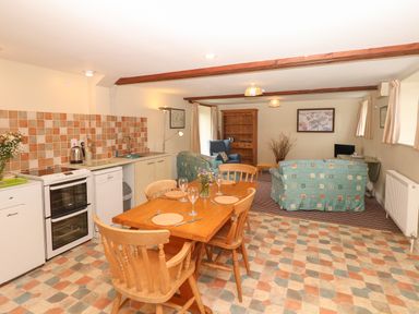 An open plan kitchen and living area with a wooden dining table set and two sofas at The Linney in Colyton