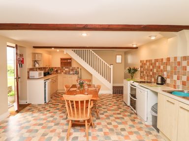 A kitchen with a dining table and wooden chairs under a staircase at The Linney in Colyton