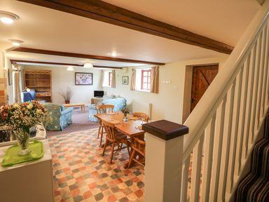 An open plan living and dining area with a wooden dining table and chairs a kitchen counter with flowers and a seating area with blue armchairs at The Linney in Colyton