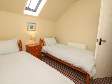 A bedroom with two single beds and a wooden nightstand with a lamp under a skylight at The Linney in Colyton