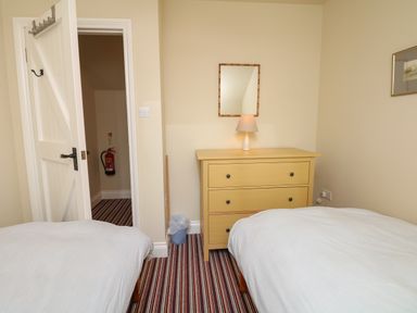 A bedroom with two single beds a yellow chest of drawers a lamp and a mirror on the wall at The Linney in Colyton