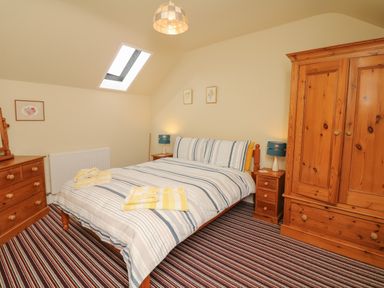 A bedroom with a double bed striped bedding wooden wardrobe and chest of drawers at The Linney in Colyton
