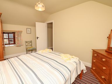 A bedroom with a bed striped bedspread wooden dresser with mirror green chair and small window at The Linney in Colyton