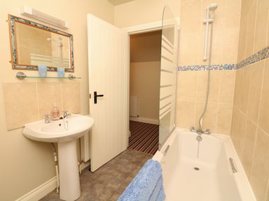 A bathroom with a pedestal sink a mirror a bathtub with a shower and a blue towel at The Linney in Colyton