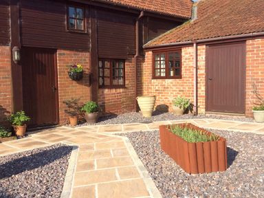 A courtyard with brick walls and wooden doors and windows with plants in pots at Battens in Colyton