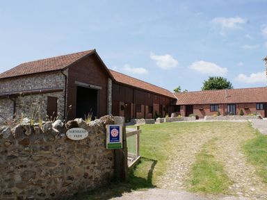 A farmyard with stone and brick buildings and a gravel driveway at Northleigh Farm in Colyton