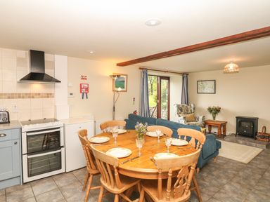 A kitchen and dining area with a wooden dining table and chairs a blue sofa a patterned armchair and a small black stove at Battens in Colyton