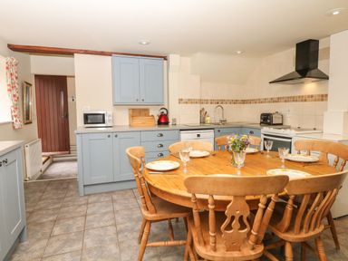 A kitchen with blue cabinets a wooden dining table set with plates and glasses and a flower vase at Battens in Colyton