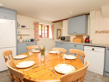 A kitchen with a wooden dining table set with plates and glasses and blue cabinets at Battens in Colyton