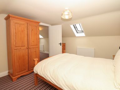 A bedroom with a wooden wardrobe, wooden bed with striped bedding, skylight window, and striped carpet at Battens in Colyton