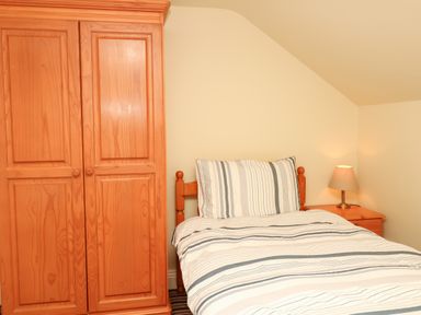 A bedroom with a wooden wardrobe a single bed with striped bedding and a nightstand with a lamp at Battens in Colyton