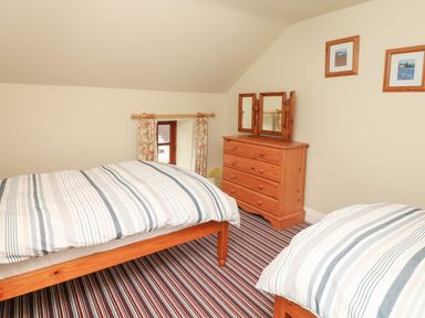 A bedroom with two beds striped bedding a wooden chest of drawers with a three-panel mirror and two framed pictures on the wall at Battens in Colyton