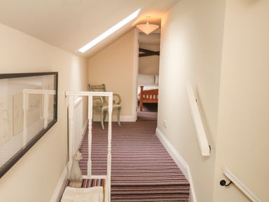 A narrow hallway with striped carpet leading to a bedroom with a wooden bed a green chair and a skylight window at Battens in Colyton