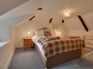 A bedroom with a double bed a checkered blanket bedside tables and sloped ceiling beams at Lew Quarry Cottage Lewdown
