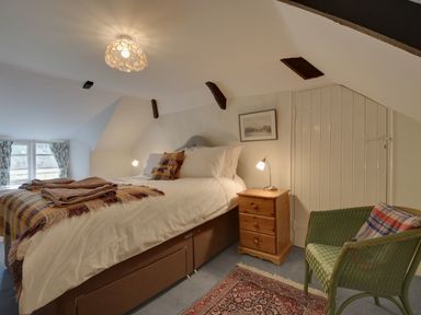 A bedroom with a double bed bedside table armchair and small window at Lew Quarry Cottage Lewdown