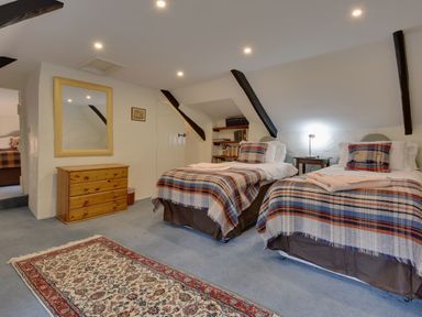 A bedroom with two single beds with plaid blankets a wooden dresser a mirror and a patterned rug at Lew Quarry Cottage Lewdown