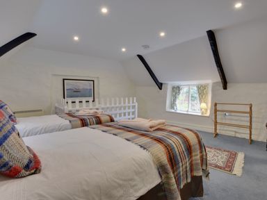 A bedroom with two single beds a window with floral curtains and a wooden drying rack at Lew Quarry Cottage Lewdown