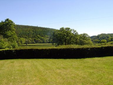 A grassy lawn with trees and hills in the background at Lew Quarry Cottage in Lewdown