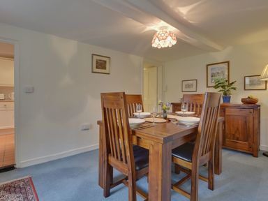 A dining room with wooden table and chairs set for four with plates and wine glasses at Lew Quarry Cottage in Lewdown