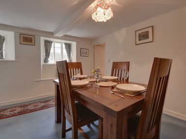 A dining room with a wooden table set for four and framed pictures on walls at Lew Quarry Cottage in Lewdown