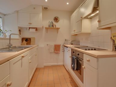 A kitchen with white cabinets a stainless steel sink oven stovetop and tiled floor at Lew Quarry Cottage in Lewdown