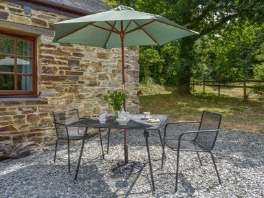 An outdoor patio area with a metal table and chairs under a green umbrella next to a stone building at Miners Dry in Gulworthy near Tavistock