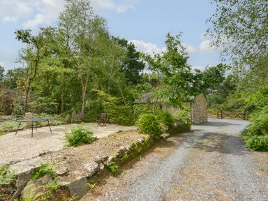 An outdoor area with gravel seating and a stone building near trees at Miners Dry in Gulworthy near Tavistock