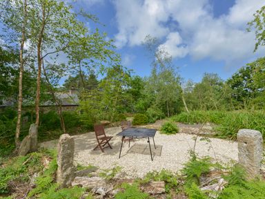 An outdoor seating area with two chairs and a table on gravel surrounded by trees at Miners Dry in Gulworthy near Tavistock