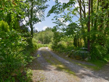 A gravel driveway surrounded by trees and green foliage with a miners dry sign on the right at Miners Dry in Gulworthy near Tavistock