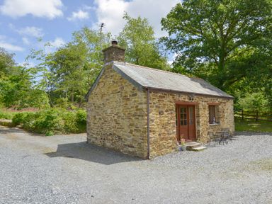 A small stone cottage with a slate roof surrounded by trees and gravel at Miners Dry in Gulworthy near Tavistock