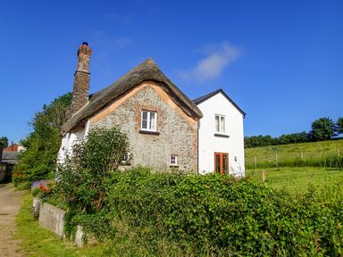 A thatched roof cottage with brick chimney and garden hedge at West Henstill House in Sandford Devon